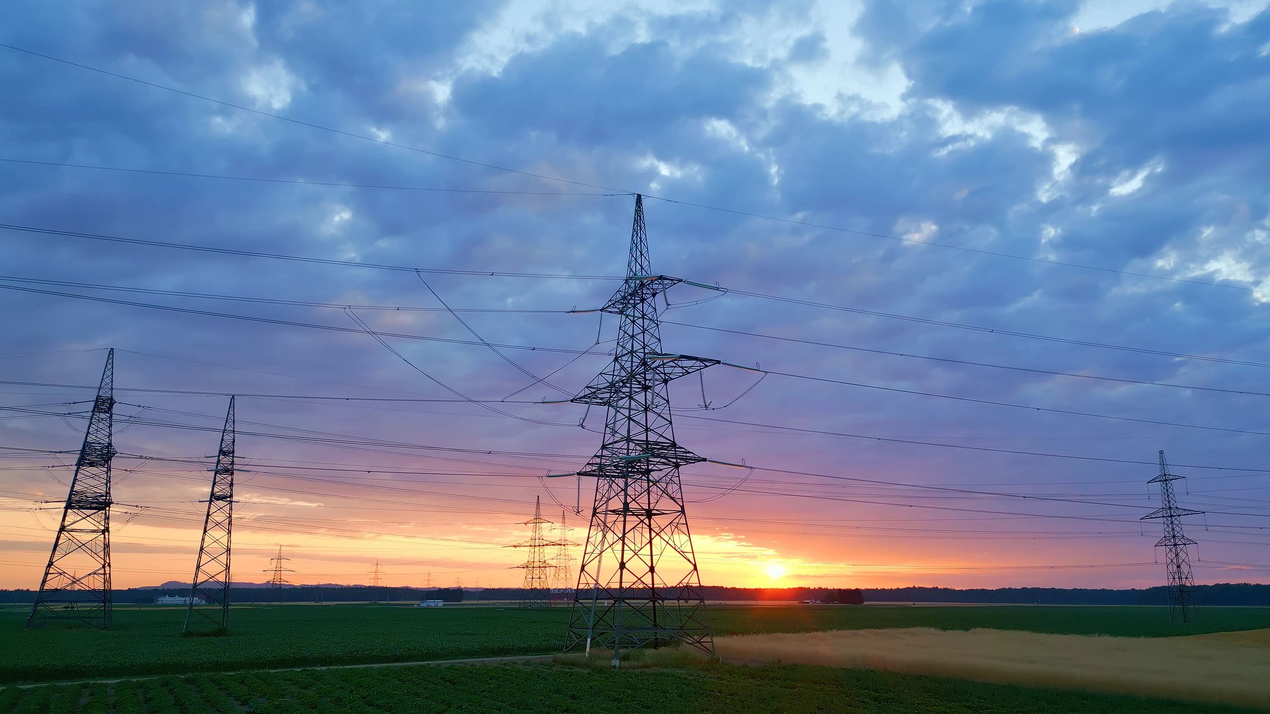 Power lines and pylons silhouetted against sunset